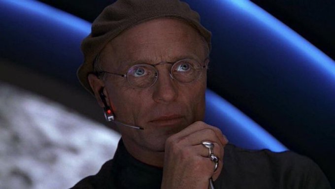 A thoughtful man wearing a cap, round glasses, and an earpiece rests his chin on his hand adorned with silver rings, appearing contemplative against a blue-lit background. The image's pensive mood echoes the post's strategic optimism about Litecoin ($LTC), suggesting a careful believer weighing the cryptocurrency's resilience despite market challenges, confident in its long-term value reaching $50.