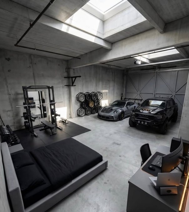 A sleek industrial-style garage featuring a home gym with squat rack and weights on the left, a low platform bed in the foreground, and a workstation with monitors on the right, alongside a gray Porsche and a black Dodge Charger parked in the center—embodying the "all u need" lifestyle of fitness, automotive passion, and minimal living.

No visible text, numbers, tickers, or names appear in the image.