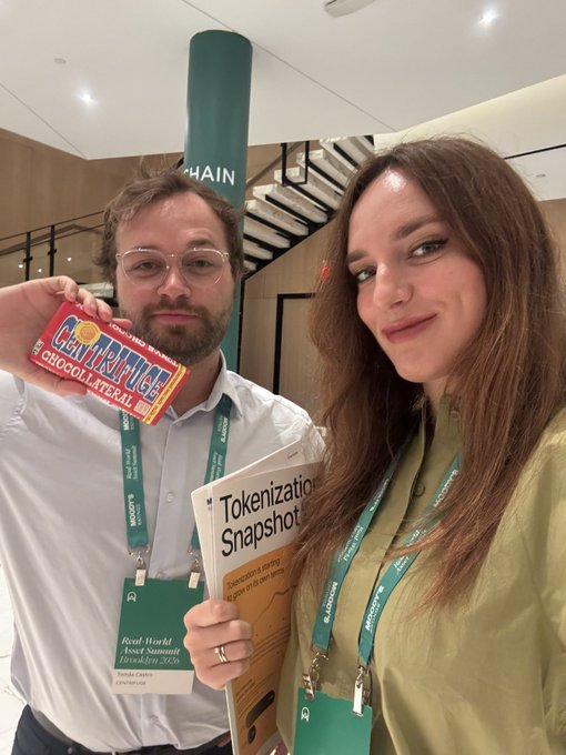 A man holds a 'Centrefill' chocolate bar while standing next to a woman holding a 'Tokenization Snapshot' booklet; both wear lanyards at an industry event.