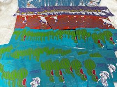 A collection of hand-painted artwork on paper showing rows of blue, green, and red figures, with some smaller white skulls or faces visible along the edges.