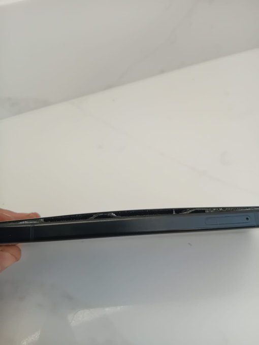 A close-up view of the bottom edge of a smartphone held in someone's hand, revealing the speaker grilles, charging port, and some white residue or damage along the edge.