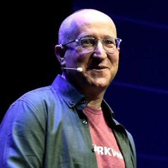 A bald man with glasses and a headset microphone is giving a presentation, with partial text "RKW..." visible on his red shirt under a denim overshirt. The image aligns with the post's mention of Eli Ben-Sasson, the Zcash co-founder, shown speaking publicly as referenced in the discussion about Bitcoin.