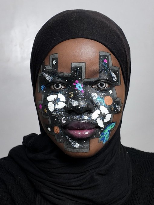 A close-up portrait of a Black woman wearing a black hijab, featuring intricate cosmic-themed face paint covering her nose and cheeks with stars, planets, and geometric patterns.