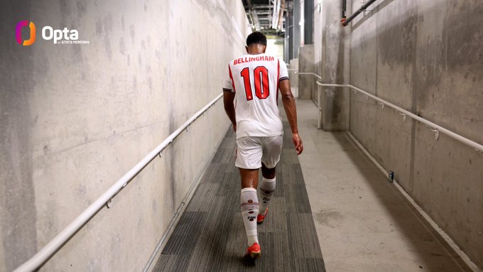 The image shows a soccer player wearing a white jersey with red lettering walking down an indoor hallway, possibly towards a match or practice session. The player's number 10 can be seen on his jersey. In the background of the image, there is text that reads "OPTIA", which might indicate the source of the image or some other information related to the soccer event.