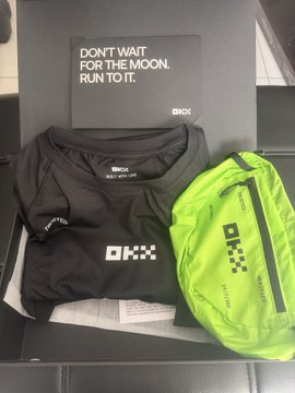 A pair of black OKX-branded running shorts and a bright neon green drawstring bag sit in front of a motivational sign reading "DON'T WAIT FOR THE MOON. RUN TO IT."