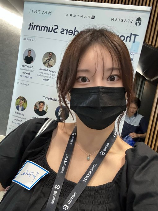 A young woman wearing a black face mask takes a selfie at what appears to be a Singapore FinTech Festival event, with a name badge reading 'Julie' visible on her chest.
