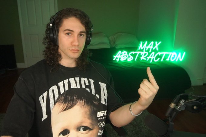A man wearing headphones and a 'YOUNG LA' graphic t-shirt points his finger up next to a glowing green neon sign that reads 'MAX ABSTRACTION'.