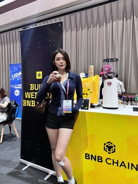 A woman enjoys a coffee at the BNB Chain booth, featuring banners that say "BUILD WITH BNBCHAIN" and "BNB CHAIN" prominently. This image visually represents the coffee break and the BNB Chain presence mentioned in the accompanying post.