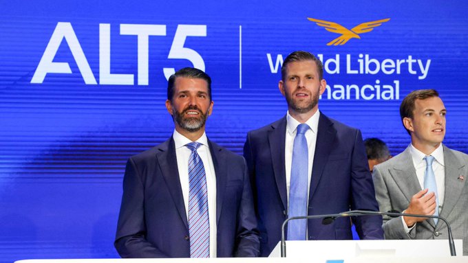 Donald Trump Jr., Eric Trump, and a third man stand at a podium at an ALT5 Sigma event promoting World Liberty Financial (WLFI), the crypto project that raised $550 million in its token sale to bring institutional capital to the digital asset market.