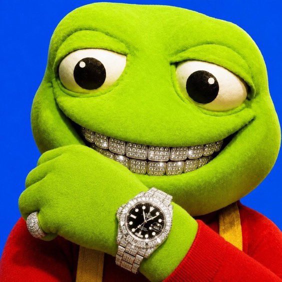 A green Pepe the Frog plush against a blue background wearing a diamond-encrusted grill and a diamond-covered Rolex watch.