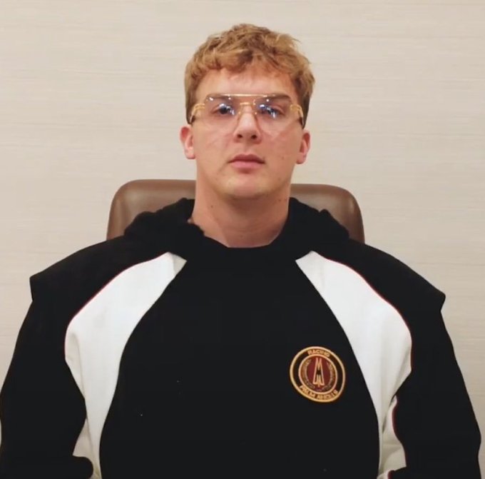 A young man with curly blonde hair and clear-framed glasses wears a black and white hoodie featuring the "Mоnolith" logo, seated against a plain wall — the image is presented in connection with Hayden Davis, the figure named in the accompanying post who allegedly launched the LIBRA memecoin endorsed by Argentina's President Milei and profited approximately $100 million as insiders drained $87M from liquidity pools.