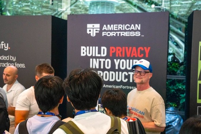 A photograph taken at a trade show booth for 'American Fortress', with a large banner reading 'BUILD PRIVACY INTO YOUR PRODUCT'.