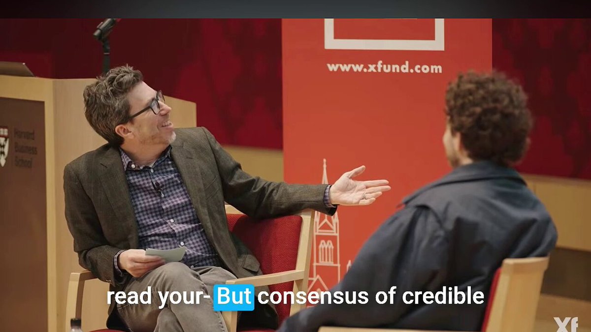 The image shows two men sitting next to each other with one man holding a book titled "Read Your Own" while they are having a conversation. The background of the image features an orange banner that says "www.xfund.com".