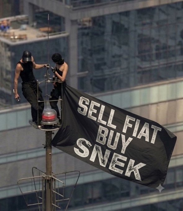 Two people in black masks and clothing standing on a high platform attaching a large black banner that reads 'SELL FIAT BUY SNEEK' near an antenna structure.