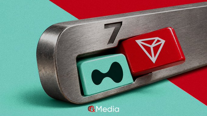 A stylized 3D rendering displays a metallic device with a teal keyhole-shaped button and a red button marked with a white triangle, featuring the number '7' and an 'IQ Media' logo.
