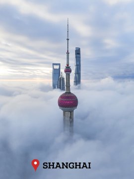 An aerial view of Shanghai's Oriental Pearl Tower and skyscrapers emerging from thick clouds, with a red location pin and 'SHANGHAI' text at the bottom.