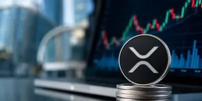 A stack of coins topped with an XRP logo sits in front of a laptop displaying a rising price chart, visually reinforcing the bullish prediction that XRP will drive tokenization to a $1,000 price target.