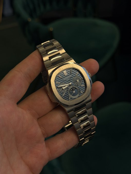 A close-up of a hand holding a luxury gold and steel watch with a blue wave-patterned dial, appearing to be an Audemars Piguet.