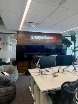 The image shows an office space with a desk area featuring two computer monitors, three chairs, and a large screen TV mounted on the wall above them. The room also has a gray bean bag chair placed near one of the desks. A whiteboard is present in the background, suggesting that this workspace could be used for brainstorming sessions or collaborative projects.

The post about the @solana network is related to the office space because it promotes the use of the @Superteam network as an alternative work environment. The image implies a modern and comfortable setting where employees can collaborate effectively using their computers, TVs, and bean bag chairs.
