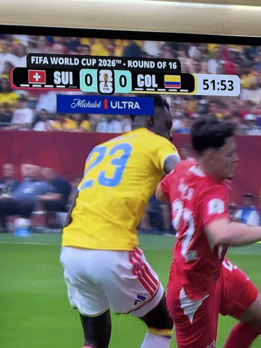 A photo of a TV screen showing a FIFA World Cup 2026 Round of 16 match between Switzerland (SUI) and Colombia (COL) tied 0-0 at 51:53, with a Swiss player (#23 in yellow) battling a Colombian player in red—the ticker "SUI" humorously resembling the stock symbol $SUI.