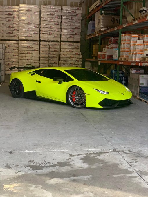 A vibrant neon yellow Lamborghini Huracán with black wheels and red brake calipers is parked inside a warehouse, surrounded by stacked inventory on industrial shelving, including boxes marked "ABC" and "118." The bold "Thank you $PAID" caption celebrates the successful sale of the eye-catching exotic supercar.