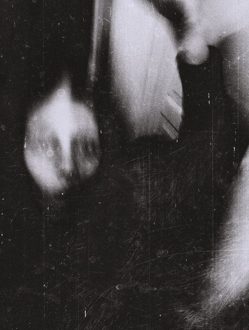 A grainy, high-contrast black and white abstract image that appears to show distorted human faces or forms emerging from darkness with scratch marks on the surface.