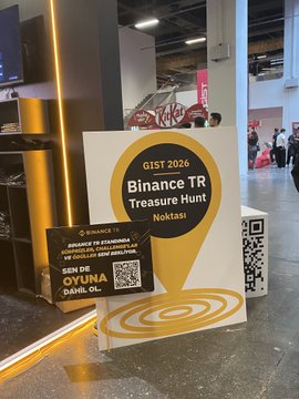 A photo shows a GIST 2026 "Binance TR Treasure Hunt" booth in Nokta, featuring a large yellow sign and a smaller placard that reads "SEN DE OYUNA DAHİL OL!" (Join the Game!) with a QR code, directly supporting the post's call to action for attendees to visit the Binance TR area, collect their stamp, and complete the treasure hunt challenge at the event.