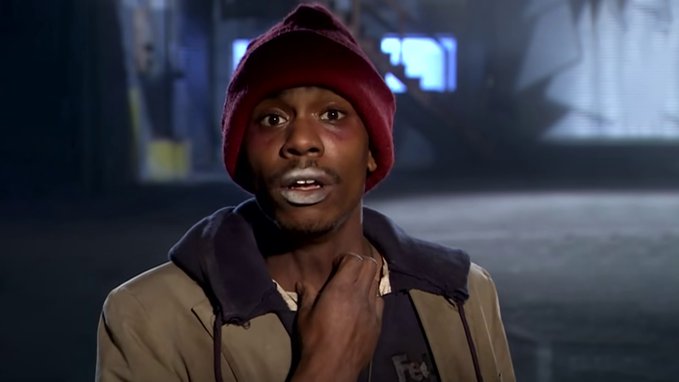 Reaction-style meme image of a young man wearing a red beanie and tan hoodie with a shocked or awestruck expression, hand near his neck, in a dark indoor setting.