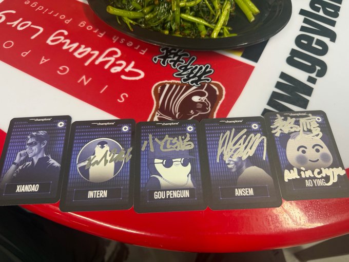 Five 'Champion' cards are arranged in a row on a Pangako sa Pagkain, Pangako sa pag Bridge table, labeled XIANDAO, INTERN, GOU PENGUIN, ANSEM, and a panda chef mascot Minacypo, with a plate of stir-fried greens visible above.