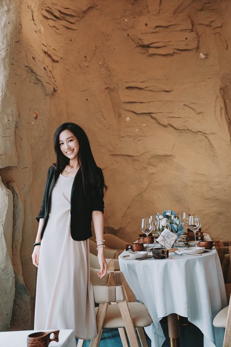 A woman in a white dress and black blazer smiles beside an elegantly set table in a sandstone alcove, complementing the post's warm, seasonal gathering mood.