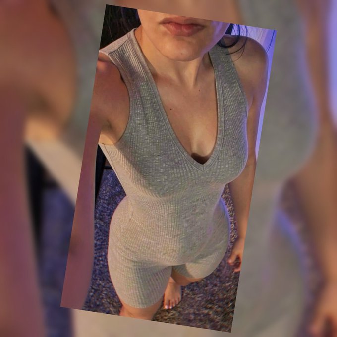 A photo taken from a high angle showing a woman wearing a form-fitting gray ribbed v-neck sleeveless dress, with her face partially cropped out of the frame.