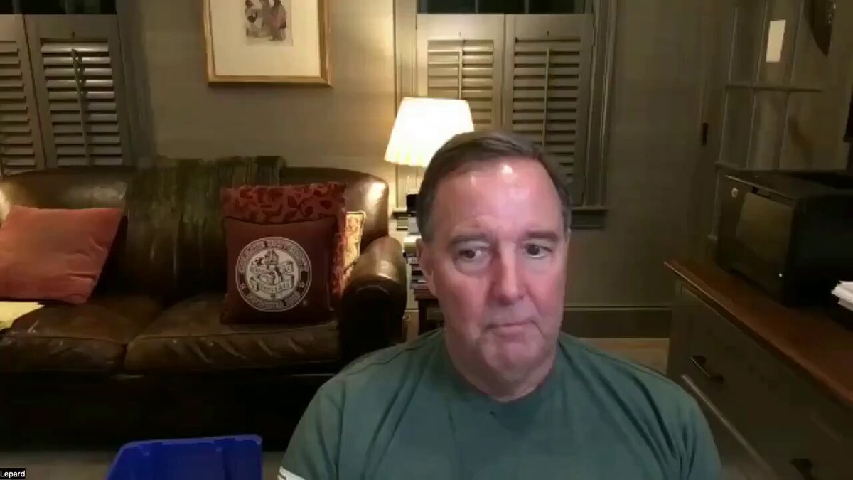 The image features a man sitting at his desk with a laptop computer in front of him, as he appears to be taking part in an online video call. The background shows a living room area which includes a couch, chair, lamp, and other items such as books on the shelves or table nearby. The text from the post about Jerome Powell talks about Bitcoin being undervalued by $450 trillion, implying that it might not be worth much due to its current price. This information is relevant to the image since the man could be a user of Bitcoin who may have been discussing this topic during his video call with someone else in the living room.