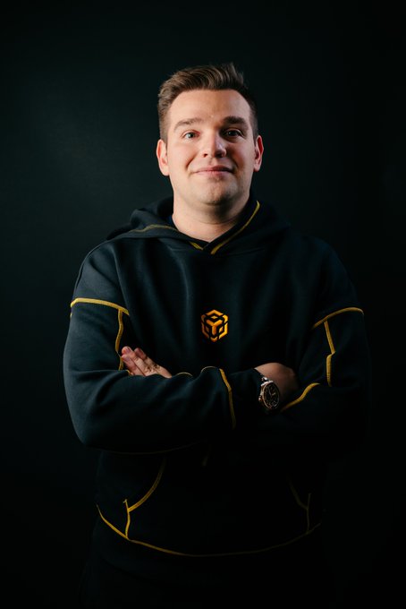 A man with crossed arms poses confidently against a dark background, wearing a black hoodie with gold trim featuring the BNB Chain logo. The post celebrates his 4-year journey as a BNB Chain LATAM Ambassador, showcasing the new merchandise that represents his ongoing dedication to the ecosystem since the Martian Program.