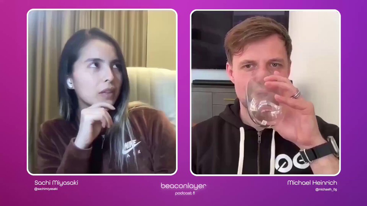 The image shows a man and woman sitting next to each other at a table with wine glasses in front of them. The woman appears to be thinking while the man is drinking from his glass, possibly engaged in conversation or contemplating something. The background features a purple wall that complements the purple screen behind them.