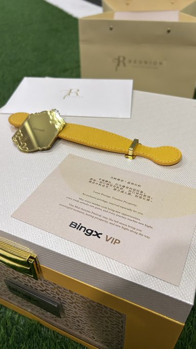 A Reunion branded VIP package with a yellow leather strap and gold charm, along with a handwritten-style note card labeled 'Bingx VIP' sitting on a display box.
