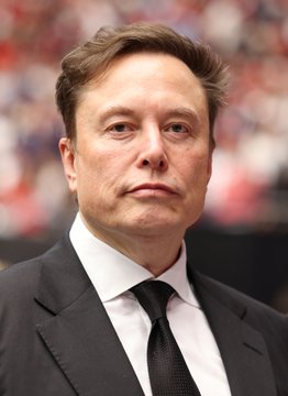A man in a black suit and tie is pictured at what appears to be a public event, identified by the accompanying post as Elon Musk. The image relates to the post's claim about SpaceX's reported Bitcoin holdings, using his likeness to underscore the bold statement that he may indirectly expose American youth to cryptocurrency.