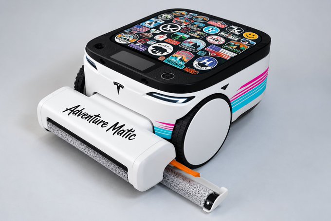 A 3D render of a small, boxy, white wheeled robot covered in stickers, with blue eyes, pink and blue racing stripes, and a cylindrical attachment labeled 'Adventure Matic' dispensing a rolled paper.