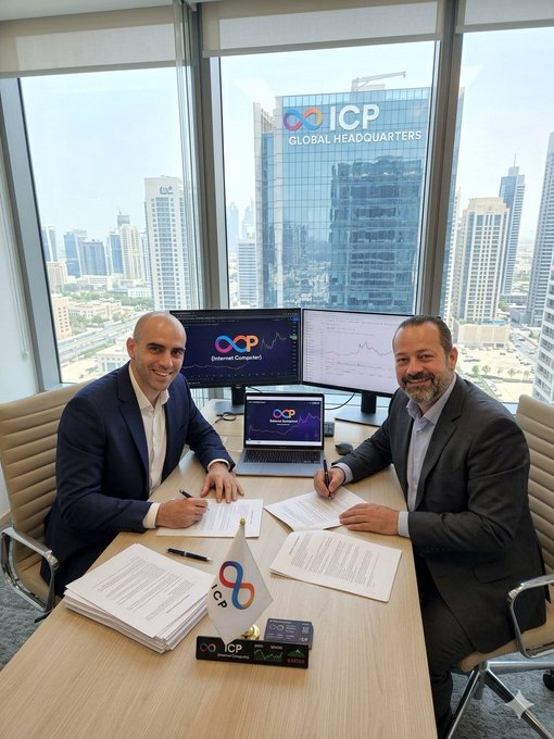 The image shows two men sitting at a desk with paperwork in front of them, possibly discussing business matters or signing documents related to cryptocurrency. The office has large windows that provide an impressive view of the city skyline outside. One man appears to be wearing a suit while the other is dressed more casually. They are surrounded by various pieces of paper and electronic equipment on the desk, suggesting they might be involved in financial transactions or planning for future investments.