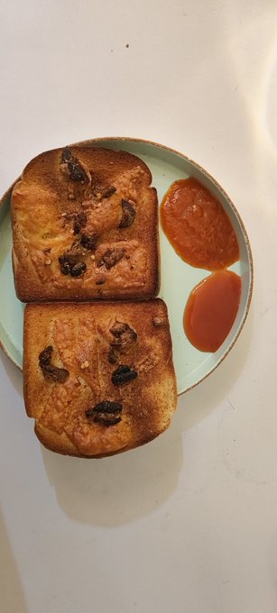 A top-down view of a light green plate holding two slices of raisin bread or French toast alongside two dollops of red ketchup on a white surface.