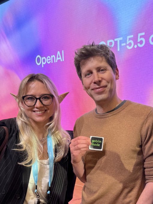 The image features a man wearing glasses holding up a small square sign with the words "OpenAI" written on it, along with an "i" for "idea". The background of the photo shows a purple wall with a banner that reads "OPEN AI", and there is also a woman standing next to him. The image seems to be related to a post about OpenAI or artificial intelligence, possibly discussing its IPO plans or highlighting its achievements in the field.