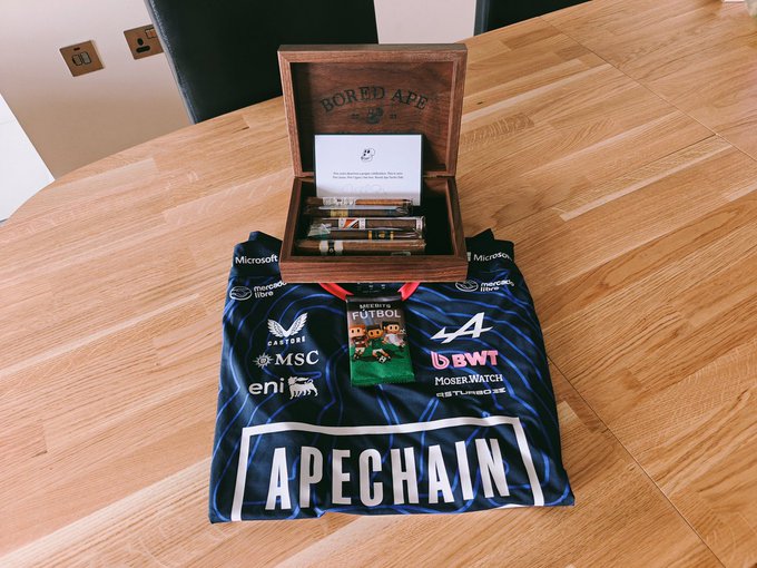 A wooden 'BORED APE' cigar box sits on an Inter Milan soccer jersey with 'APECHAIN' printed on it, alongside a commemorative collectible card featuring Pepe the Frog.