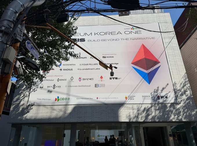 An Ethereum Korea One event billboard with the tagline 'BUILD BEYOND THE NARRATIVE' is displayed on a building, featuring sponsor logos including Optimism, KODA, NODEINFRA, FOUR PILLARS, EigenLayer, KOREA, RADIUS, Undefined Labs, and DB저축은행.