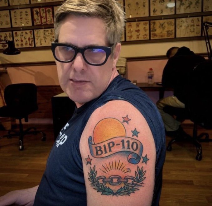 A man in glasses shows off a traditional-style shoulder tattoo featuring a banner reading "BIP-110" with a sun, stars, and chain design, visually referencing the Bitcoin Improvement Proposal mentioned in the accompanying post. The image appears to be a humorous or symbolic statement about the proposal's chances of passing.