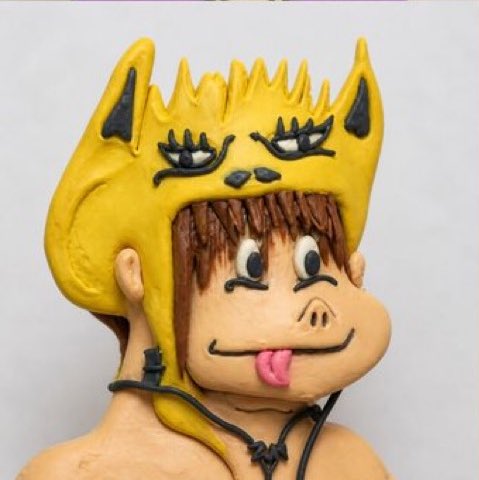 A clay figurine of a cartoonish character wearing a yellow animal-themed hood with horns, large eyes, and its tongue sticking out.
