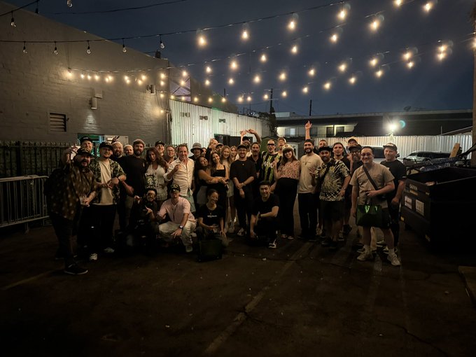A group of people pose together at night under string lights at what appears to be an outdoor venue, celebrating Bored Ape Yacht Club's "FUCK IT LA" event for the Mutants' birthday. The caption references the gathering as an incredible celebration in Los Angeles, with attendees gathered outside a building illuminated by overhead string lights.