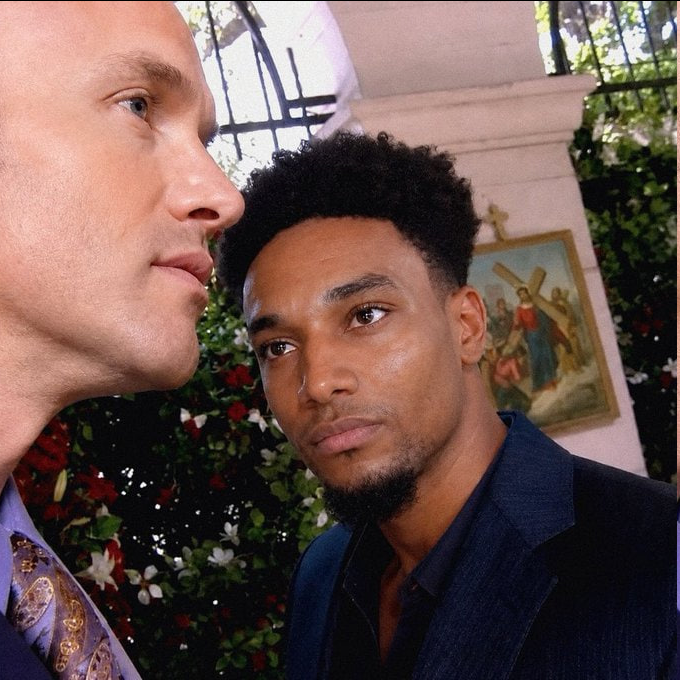Two men pose in profile next to each other, with one glancing toward the other against a backdrop of floral arrangements and a framed religious painting depicting a cross. The image accompanies a podcast promotion referencing $ANSEM, likely featuring the crypto influencer known by that handle in the discussion.