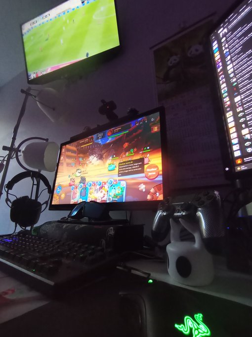 A gaming setup shows a monitor displaying a video game alongside another screen showing soccer and a third screen with chat, with a Razer keyboard visible.