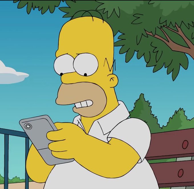 A cartoon image of Homer Simpson from The Simpsons looking at his smartphone with a worried or surprised expression while sitting on a bench.