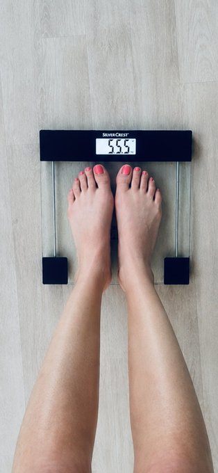 A pair of feet with red-painted toenails stand on a Silvercrest digital scale displaying "55.5" kg, perfectly capturing the "all the 5's" pattern the poster noticed. The image playfully highlights the mysterious coincidence of their weight, height (5'5"), and shoe size (5.5) all sharing the same digit.