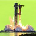 A rocket on a launch pad lifting off amid clouds of smoke and fire against a yellow sky.